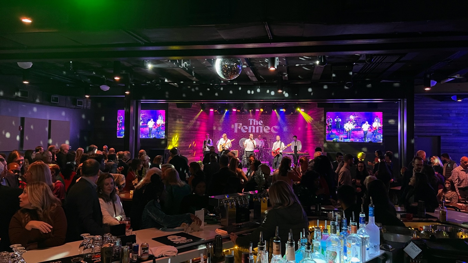 Live show at The Fennec — band, video walls, packed crowd, bar
